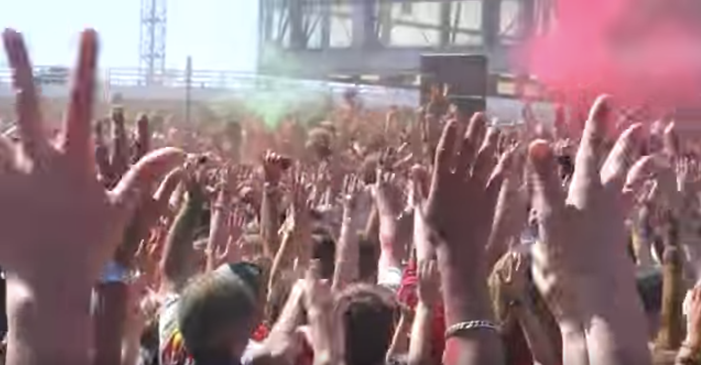 mani di una multitudine di persone alzate verso il cielo; fumogini rosa.